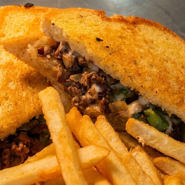 A grilled sandwich with meat, cheese, and peppers, served with golden french fries on a white plate.