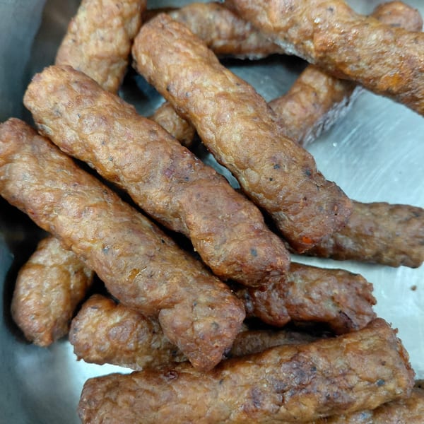 Close-up of several golden-brown fried sausage links or meat sticks in a metal container.