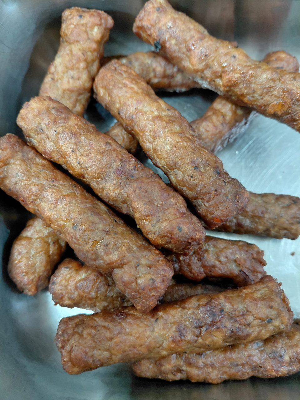 Close-up of several golden-brown fried sausage links or meat sticks in a metal container.