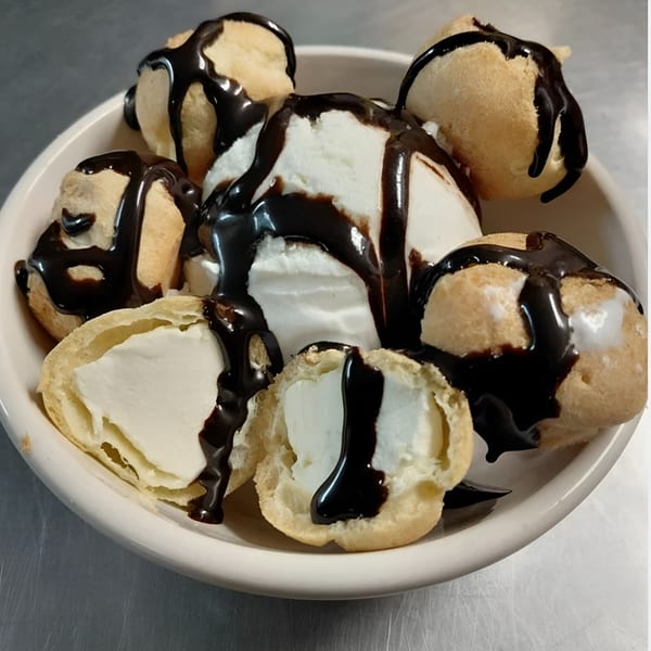 A white bowl filled with cream puffs and vanilla ice cream, drizzled with chocolate syrup.