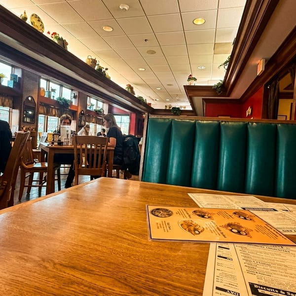 A cozy restaurant interior with red walls, green booths, wooden tables, and patrons dining.