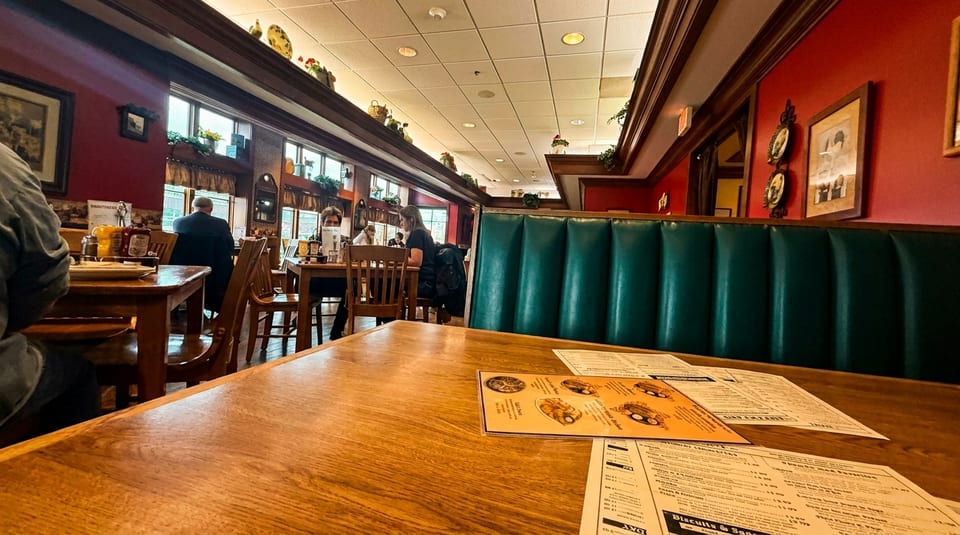 A cozy restaurant interior with red walls, green booths, wooden tables, and patrons dining.