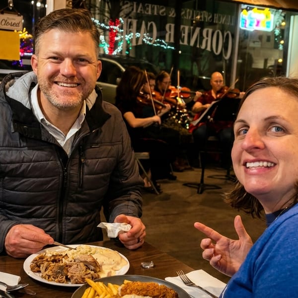 Smiling couple enjoying a meal at a restaurant with live violin music in the background.