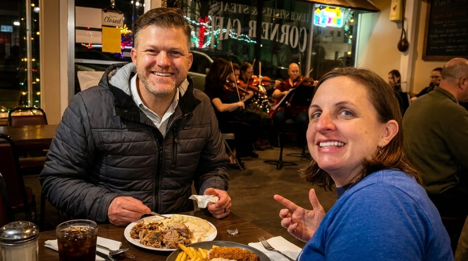 Smiling couple enjoying a meal at a restaurant with live violin music in the background.