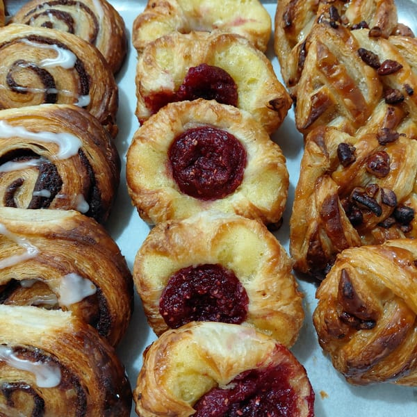 A tray of assorted pastries, including cinnamon rolls with icing, raspberry danishes, and pecan pastries.