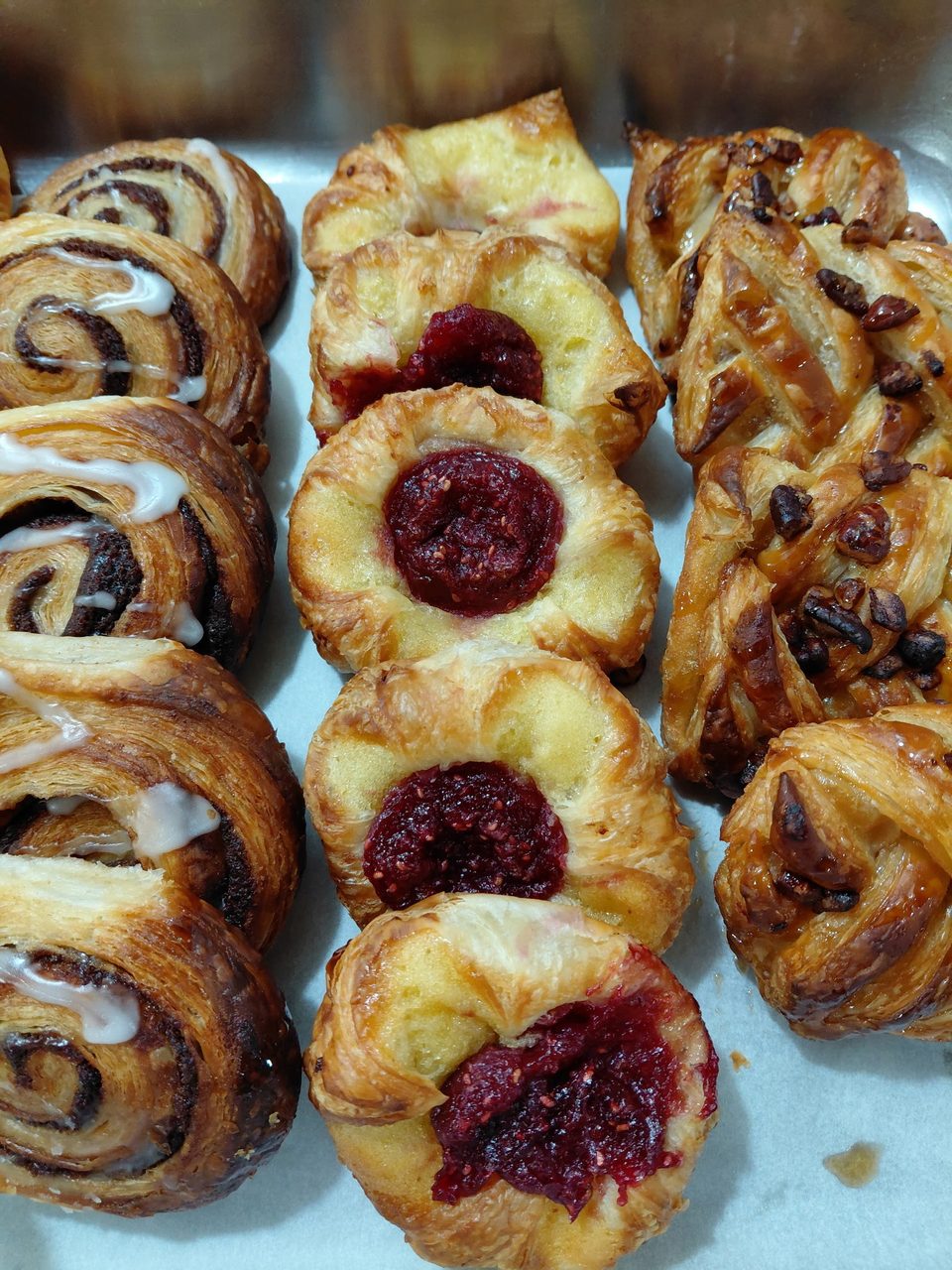 A tray of assorted pastries, including cinnamon rolls with icing, raspberry danishes, and pecan pastries.