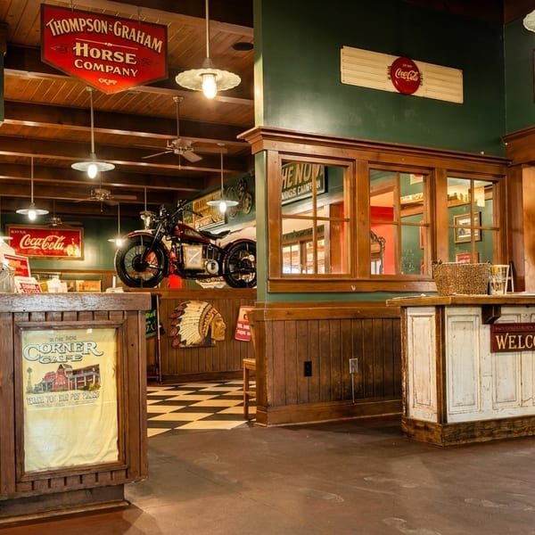 Rustic restaurant interior with wooden counters, vintage signs, a motorcycle display, and dining area.
